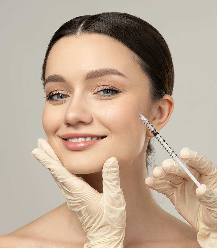 Woman smiling while gloved hands hold a Botox syringe near her cheek
